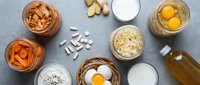 Healthy breakfast ingredients flat lay with eggs, milk, oats, nuts and supplements on gray background for nutritious morning meal preparation.