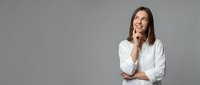 Young professional woman in white shirt thinking with hand on chin, looking up thoughtfully against gray background for business presentations.