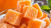 Fresh orange fruit jelly cubes coated in sugar crystals, close up macro shot showing sweet dessert texture in glass bowl with bright citrus color.