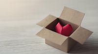 Red heart in open cardboard box on wooden surface symbolizing love delivery, gift giving, romantic surprise, care package concept.