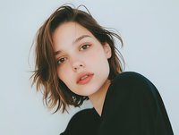 Young brunette woman with short bob haircut wearing black top against white background for portrait photography and lifestyle content.