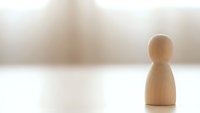 Single wooden pawn figure standing alone on white surface with soft blurred background representing isolation, leadership, individuality and minimalist concept.