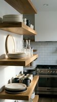Modern kitchen with floating wooden shelves displaying dishes and glassware against white subway tile backsplash for contemporary home interior design.