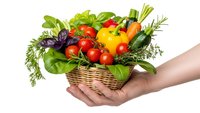 Fresh organic vegetables and herbs in wicker basket held by hands on white background. Healthy eating concept for cooking and nutrition.
