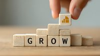Hand placing wooden block with growth chart icon above letter blocks spelling "GROW" on wooden table, symbolizing business development and progress tracking.