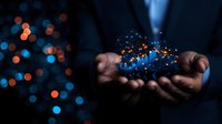 Glowing digital cloud network floating above business professional hands with blue and orange bokeh lights in dark background, representing cloud computing.