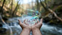 Hands holding holographic renewable energy interface with solar panels and wind turbines floating above palms in natural forest setting with waterfall.