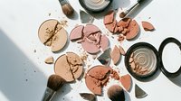 Broken makeup powder compacts and brushes scattered on white surface creating artistic beauty cosmetics flatlay composition for design projects.
