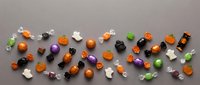 Colorful Halloween candy assortment scattered on gray background with orange, purple, green and black wrapped sweets for trick or treat celebrations.