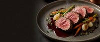 Sliced beef tenderloin with roasted vegetables and red wine sauce on dark plate, gourmet restaurant presentation for fine dining menu design.