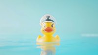Yellow rubber duck wearing white captain hat floating in bright blue swimming pool water with reflections on calm surface.