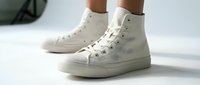 White high-top canvas sneakers worn by a person, showcasing a classic casual style on a light background, perfect for fashion and lifestyle content.