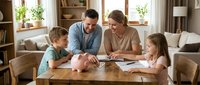 Happy Caucasian family with two children sitting at wooden table in bright living room, parents helping kids with homework and school activities at home.