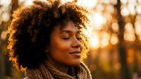 Young African American woman with curly hair enjoying peaceful moment in warm golden autumn sunlight with eyes closed and serene expression outdoors.