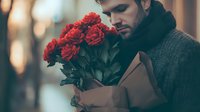 Young man in warm sweater holding bouquet of red roses against blurred bokeh background, romantic mood for Valentine's Day or anniversary celebration.