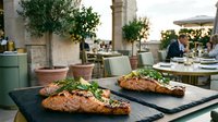Grilled salmon fillets with herbs on slate plates at upscale restaurant terrace during golden hour dining experience with elegant outdoor setting.