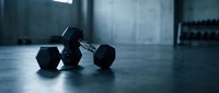 Black dumbbells arranged on a concrete gym floor with industrial warehouse setting, suitable for fitness, strength training, and workout content.