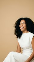 Happy young African American woman with curly hair laughing in white outfit against beige background for lifestyle and wellness content.
