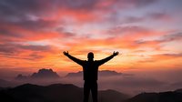 Person celebrating success with raised arms against dramatic sunset sky over mountain landscape for motivation and achievement concepts.