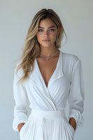 Young woman with blonde hair wearing elegant white wrap dress and silver necklace against light background, fashion portrait in natural lighting.