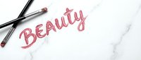 Pink handwritten word beauty with makeup brushes on white marble surface, suitable for cosmetics, skincare, and beauty industry marketing materials.