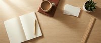 Minimalist wooden desk workspace with open notebook, coffee cup, smartphone and small plant creating clean organized office environment for productivity and focus.