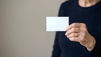 Mature man in dark sweater holding blank white business card for branding mockup and corporate identity design projects.