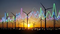 Wind turbines silhouetted against sunset sky with colorful energy wave graphics overlay representing renewable power generation and sustainable electricity.