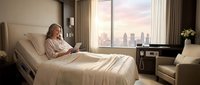 Young woman patient relaxing in modern hospital bed reading book with city skyline view during sunset recovery time in private medical room.