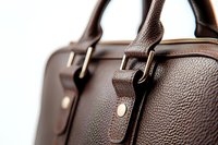 Close-up view of brown leather briefcase handle showing detailed texture, metal buckles and stitching. Luxury business accessory with selective focus on grain pattern.