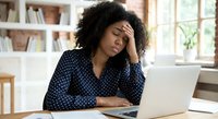 Stressed African American businesswoman with headache working on laptop at home office, experiencing work burnout and mental fatigue during remote work.