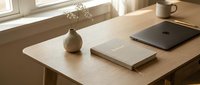 Minimalist home office desk with notebook, laptop, ceramic vase, and mug in warm natural light, cozy productive workspace.