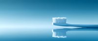 Blue toothbrush with white bristles reflected on glossy surface against turquoise background, minimalist dental hygiene concept for healthcare marketing.