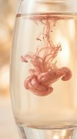 Pink ink drop dissolving in clear water glass creating fluid abstract patterns with warm golden background lighting for creative design projects.