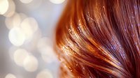 Shimmering copper red hair with golden glitter sparkles against blurred bokeh lights background, creating magical festive atmosphere for beauty and fashion concepts.