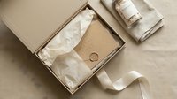 Elegant gift box with wax seal envelope, tissue paper, ribbon, and a candle on linen background, perfect for luxury packaging and branding concepts.