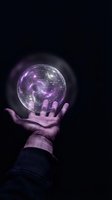 Hand holding glowing purple galaxy sphere with swirling cosmic energy and stars floating above palm against dark background for mystical designs.