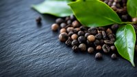 Fresh roasted coffee beans scattered on dark slate surface with green leaves for natural organic beverage concept and cafe branding materials.