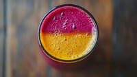 Vibrant layered smoothie with pink dragon fruit and mango creates striking two-tone effect, topped with natural bubbles, shot from above on dark wooden surface.