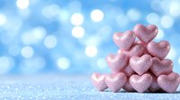 Pink glittery heart-shaped decorations stacked against soft blue bokeh background with sparkles. Romantic holiday concept for Valentine's Day and love celebrations.