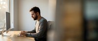 Young professional businessman working on computer at modern office desk during daytime with natural window lighting for productivity and workflow concepts.