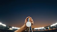 Athlete holding trophy cup overhead in stadium with bright floodlights at night, celebrating sports victory and championship success.
