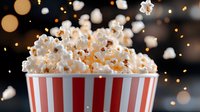 Fresh popcorn exploding from red striped container with flying kernels against dark background with golden bokeh lights, dramatic food photography.