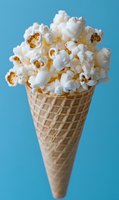 Fresh popped popcorn overflowing from waffle ice cream cone on bright blue background for creative food concept and snack advertising campaigns.