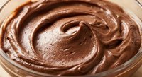 Rich creamy chocolate frosting swirled in glass bowl, smooth texture for baking desserts, cakes, cupcakes and sweet treats preparation in kitchen.