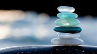 Balanced stack of smooth sea glass stones in turquoise and white tones against blurred water background, symbolizing zen, balance, and mindfulness.
