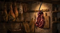 Aged meat hanging in rustic butcher shop with cured products drying on hooks, traditional charcuterie production and food preservation technique.