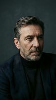 Middle-aged man with salt-and-pepper hair and beard wearing dark blazer and turtleneck against neutral backdrop. Professional portrait suitable for corporate, business, and editorial use.
