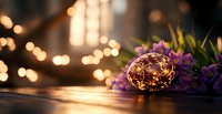 Glowing decorative egg with fairy lights and purple flowers on wooden surface against blurred bokeh background creates magical spring atmosphere.