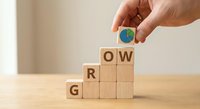 Hand placing earth globe symbol on wooden blocks spelling GROW representing sustainable business development and environmental growth strategy.